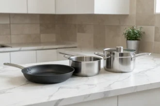 Ensemble de casseroles et poêles Elsay posé sur un plan de travail en marbre blanc dans une cuisine moderne et épurée
