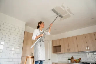 Femme utilisant un balai plafond à tête microfibre pour nettoyer un plafond de cuisine moderne